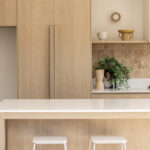 Caesarstone Snow 2141 surface in Minimalist kitchen with wooden cabinetry, white countertops, gas stove, sink, stool seating, and decorative plants.