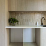 Caesarstone 2141 Snow surface in Minimalist kitchen area with light wood cabinets, white countertop, black faucet, and green plants.