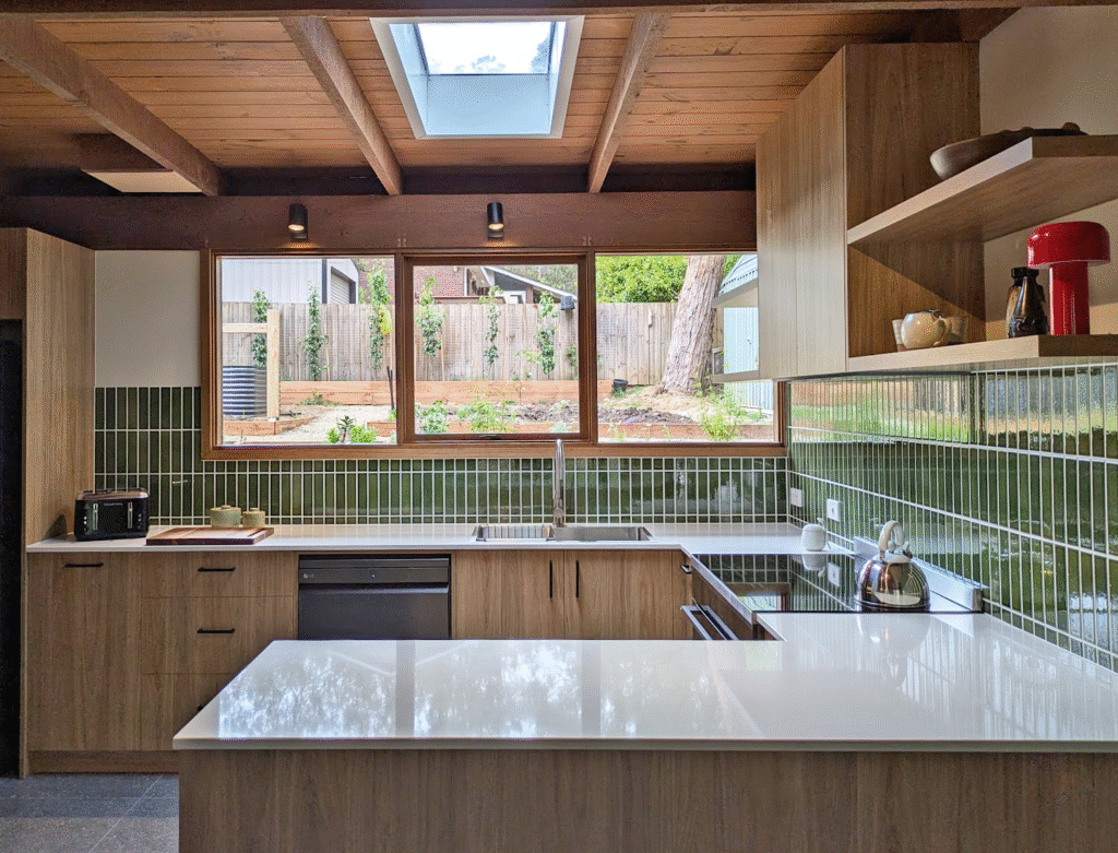 Mid century inspired, peninsula kitchen layout with Caesarstone surface benchtops, timber joinery and vertical green tile splashback, designed for practical workflow and natural light.
