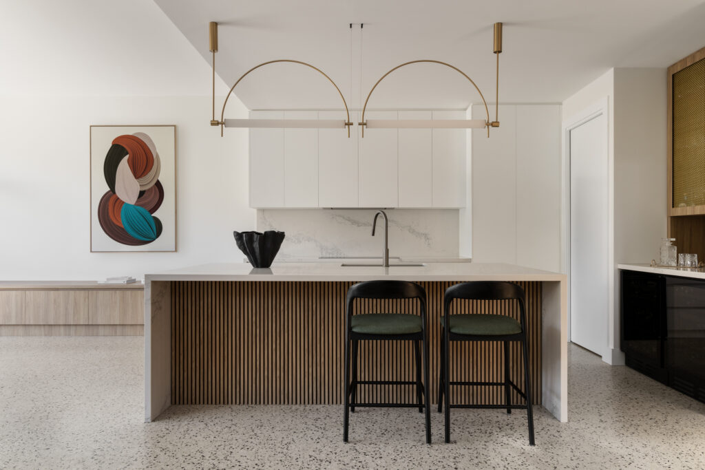 L-shaped kitchen with Caesarstone benchtops, timber-slatted island and brass pendant lighting, combining contemporary minimalism with warm texture.