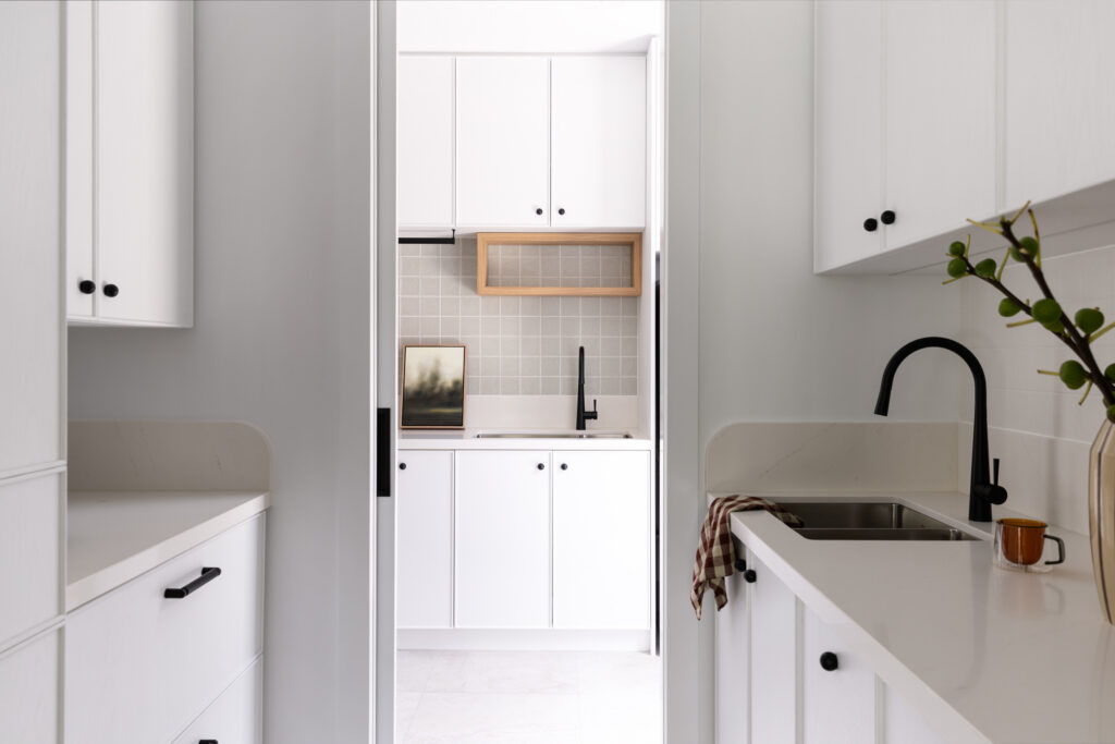 White modern laundry featuring a Galley layout and white stone benchtops with white cabinetry and black fixtures