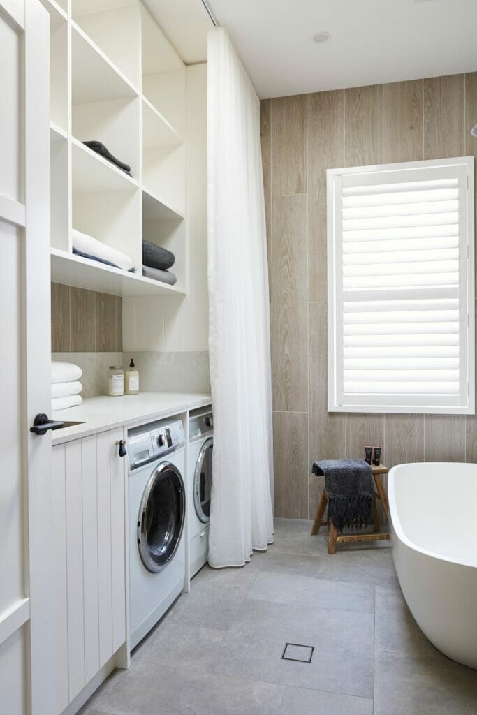 Modern laundry bathroom with white sheer curtains, white cabinets and grey tiles.