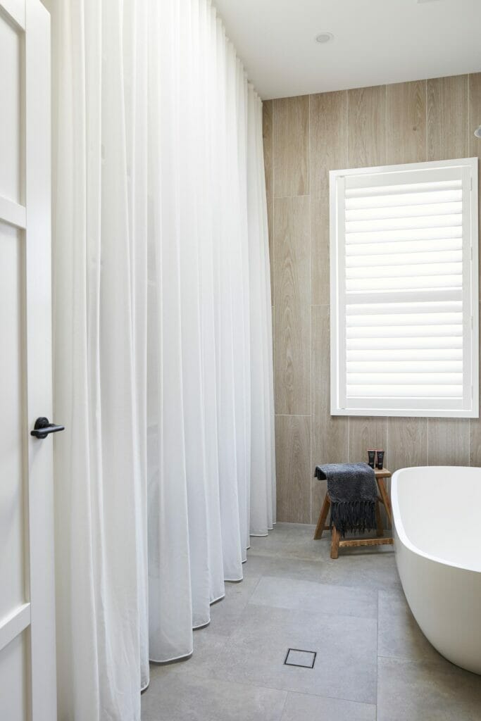 Modern laundry bathroom with white sheer curtains and grey tiles.