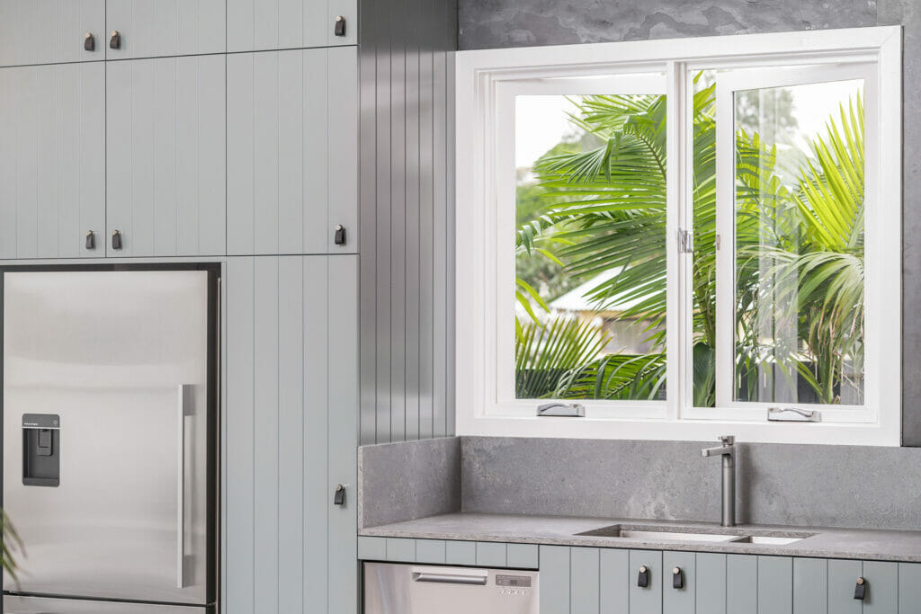 Modern kitchen with light green cabinets, stainless steel refrigerator, concrete benchtop, and white window frames.