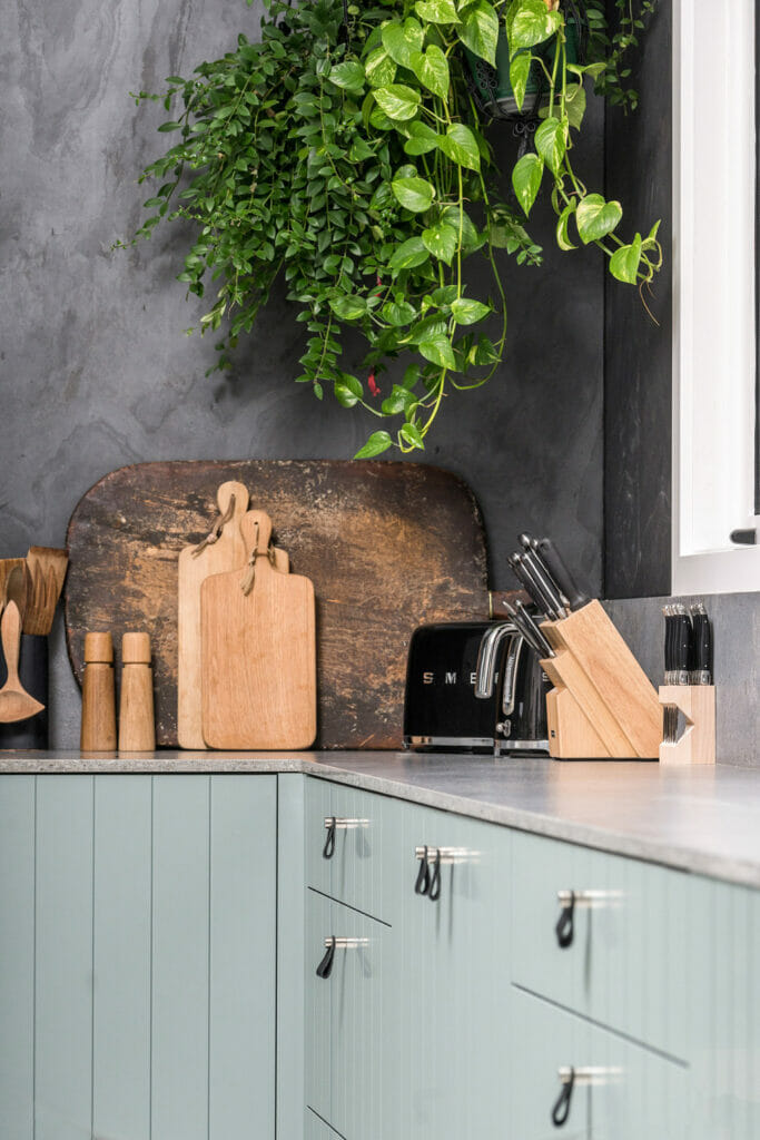 Modern caesarstone kitchen with green cabinetry, grey stone splashback, hanging plants, and concrete benchtops.
