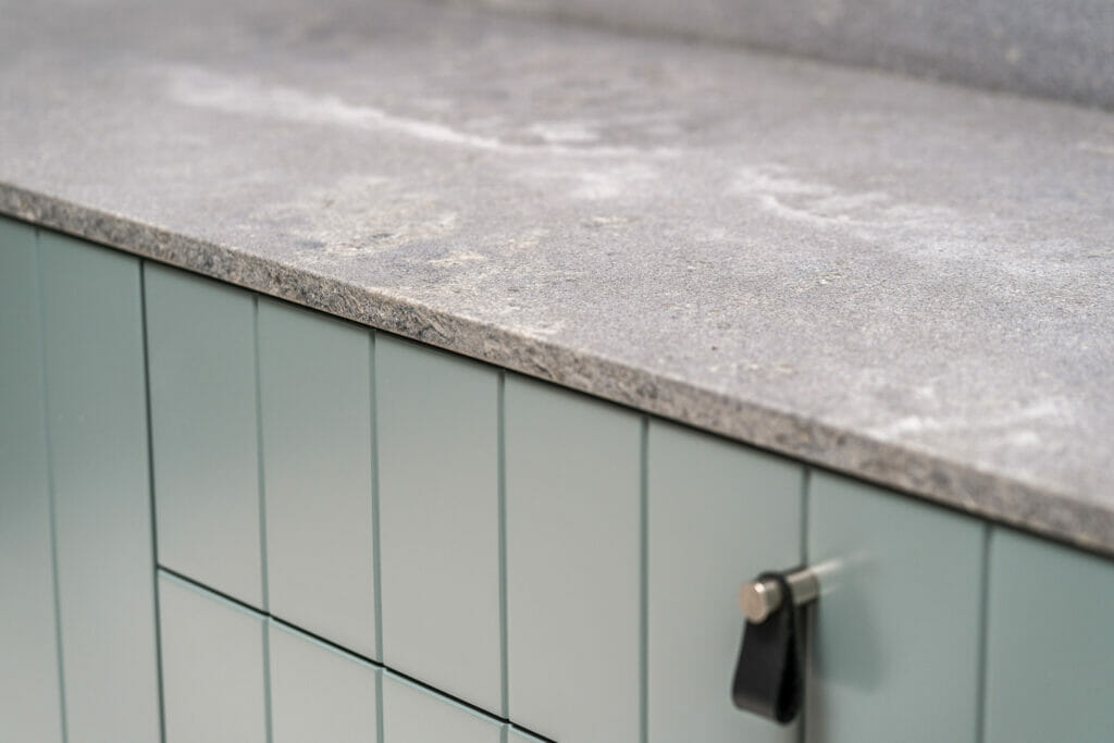 Concrete benchtop surface with green cabinets.