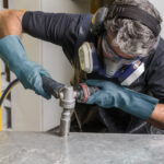 Stonemason worker safely drilling into Caesarstone benchtop with respiratory protection equipment and PPE on.