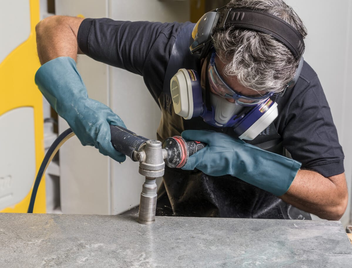 Stonemason worker safely drilling into Caesarstone benchtop with respiratory protection equipment and PPE on.