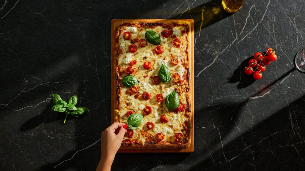 Rectangular pizza with tomato and basil, on a dark Caesarstone<sup>®</sup> Porcelain surface