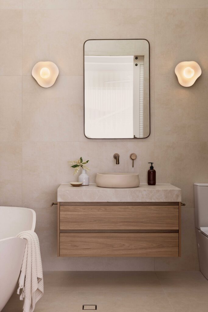 Calming bathroom retreat featuring Caesarstone<sup>®</sup> porcelain surface, paired with warm timber vanities and soft, natural finishes for a spa-inspired feel.