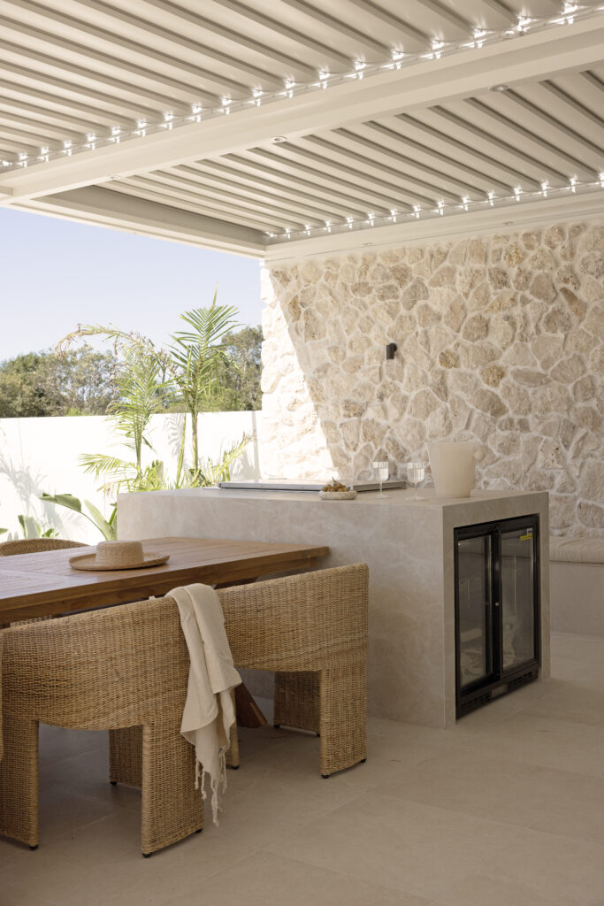 Stylish outdoor entertaining area featuring Caesarstone<sup>®</sup> porcelain surface, layered with natural stone, timber, and dappled sunlight for a resort-like ambiance.