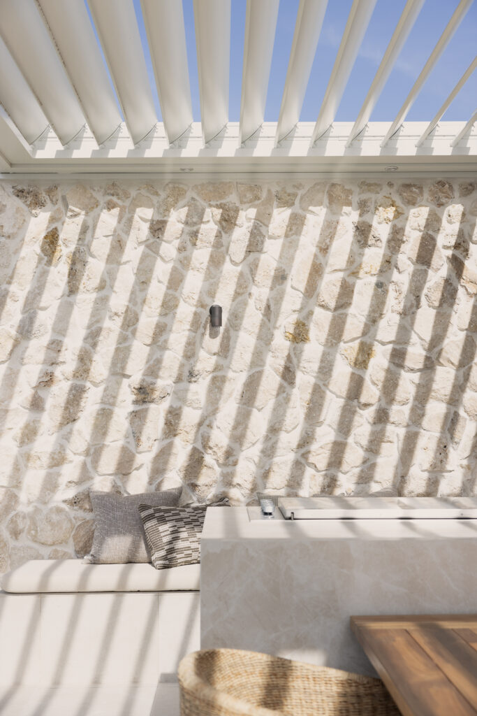 Stylish outdoor entertaining area featuring Caesarstone<sup>®</sup> porcelain surface, layered with natural stone, timber, and dappled sunlight for a resort-like ambiance.