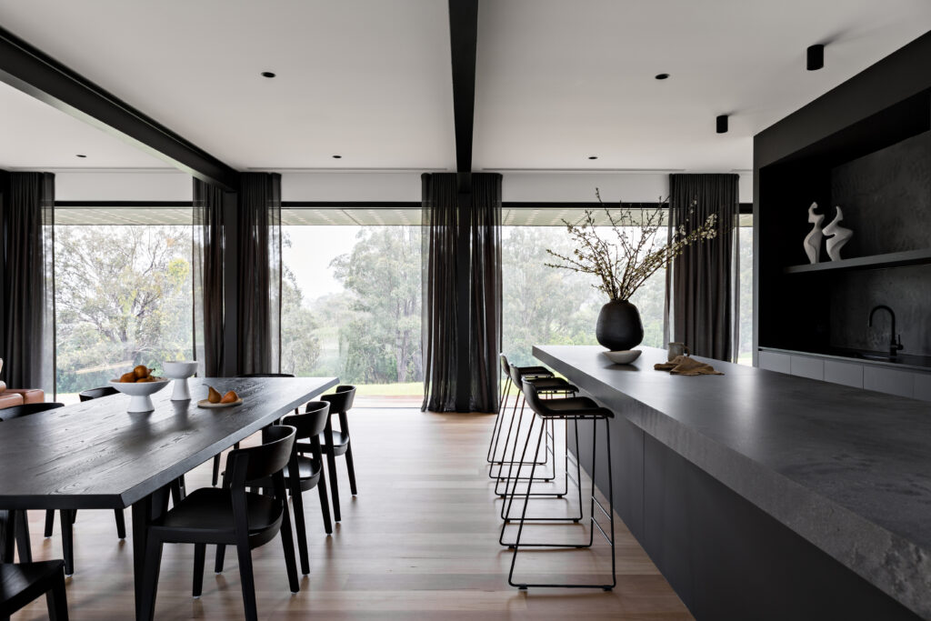Open-plan kitchen and dining space in Toby House featuring a Caesarstone<sup>®</sup> Rugged Concrete island benchtop and full-height glazing.