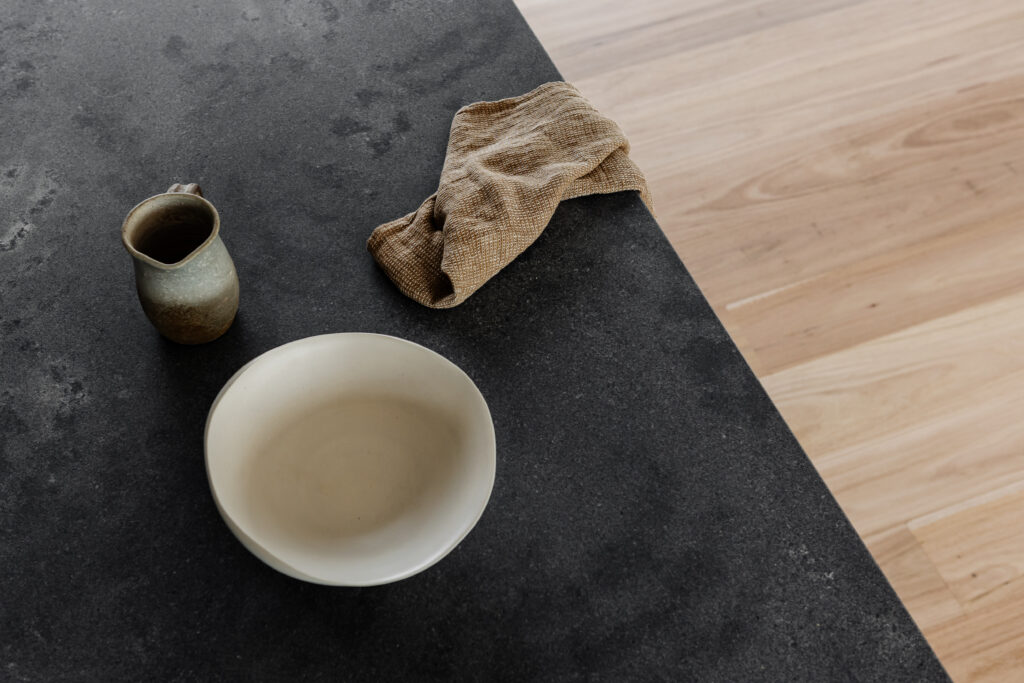 Close-up of Caesarstone<sup>®</sup> benchtop with ceramic tableware and warm timber flooring.