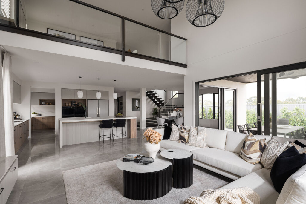 Open-plan display home featuring a Caesarstone<sup>®</sup> kitchen with island bench, butler’s pantry, and modern living area with large sectional sofa and tiled flooring.