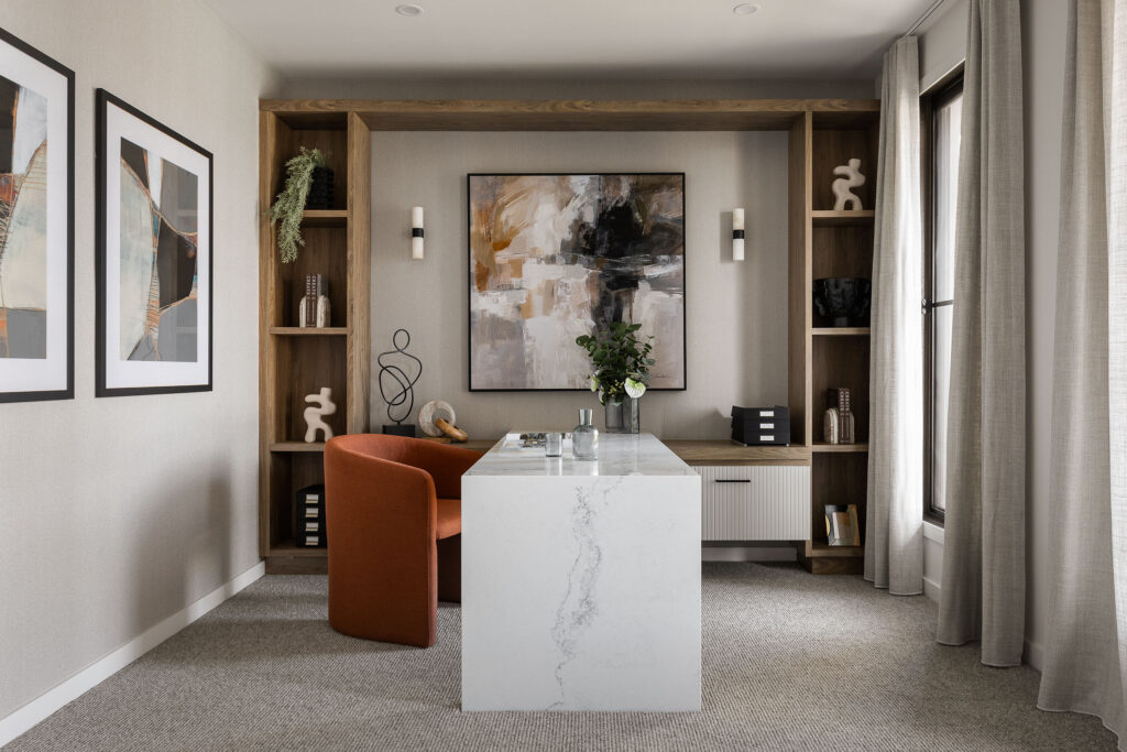 Modern home office with Caesarstone<sup>®</sup> desk, open timber shelving, abstract artwork, and a rust-coloured accent chair.