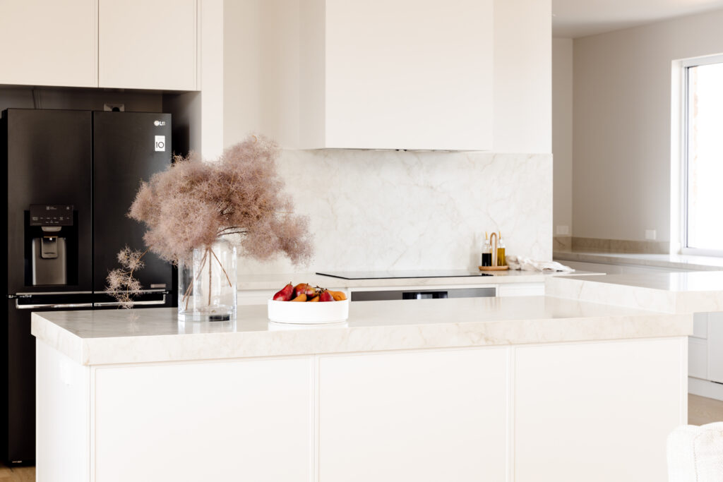 Modern kitchen with Caesarstone<sup>®</sup> benchtops and splashback, featuring integrated white cabinetry and black fridge.  