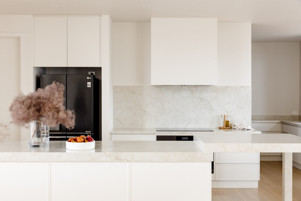 Modern kitchen with Caesarstone<sup>®</sup> benchtops and splashback, featuring integrated white cabinetry, black fridge, and custom leg island design.