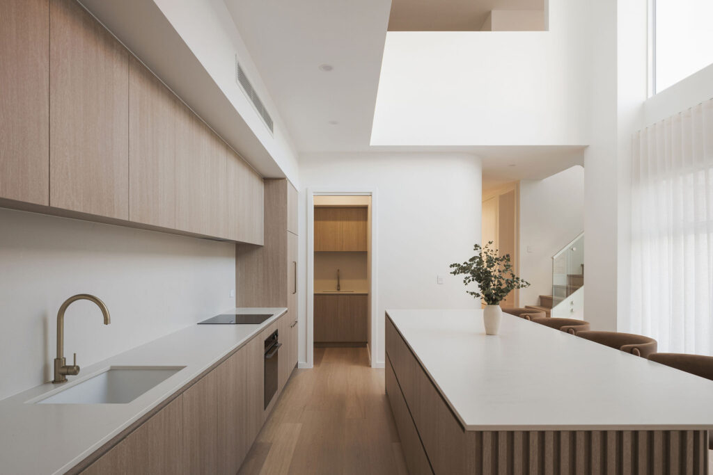 Modern kitchen with timber cabinetry, Caesarstone<sup>®</sup> benchtop, and a double-height void bringing natural light into the space.