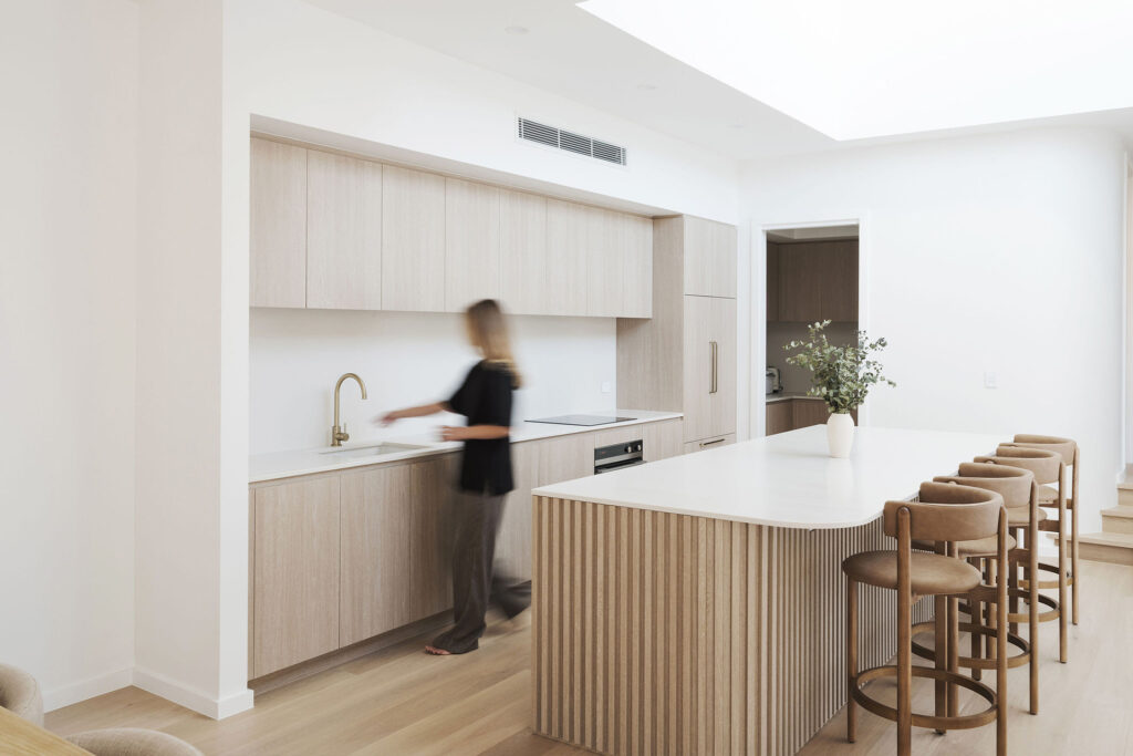 Light-filled modern kitchen with ribbed oak island and Caesarstone<sup>®</sup> benchtop beneath a double-height void.