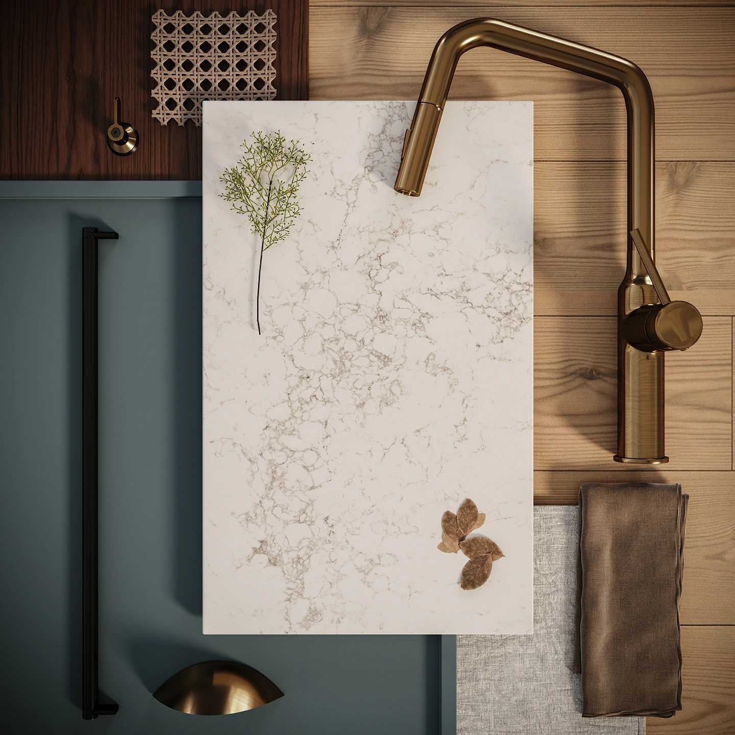 Flatlay of Caesarstone surface sample with soft brown veining, surrounded by brass tapware, timber textures, blue cabinetry panel, and natural fabric swatches.