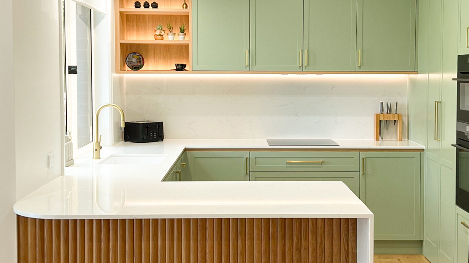 Modern peninsula kitchen with Caesarstone Snow benchtop, green cabinetry and fluted warm timber island details.
