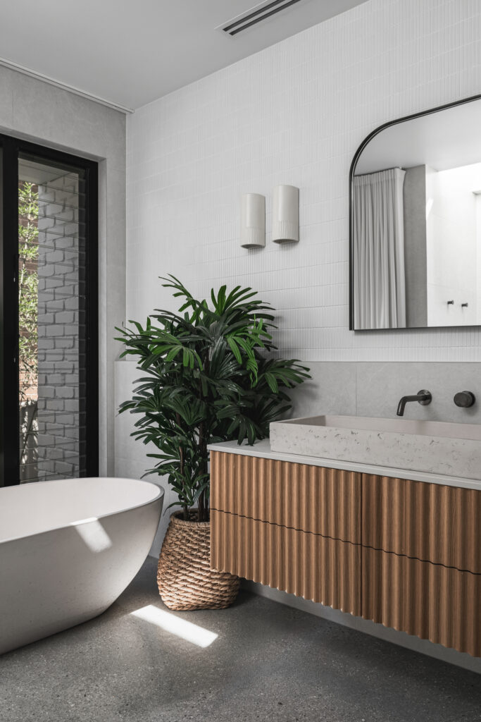 Main bathroom with Caesarstone<sup>®</sup> benchtop double vanity, ribbed timber cabinetry, freestanding bath, and soft natural light.