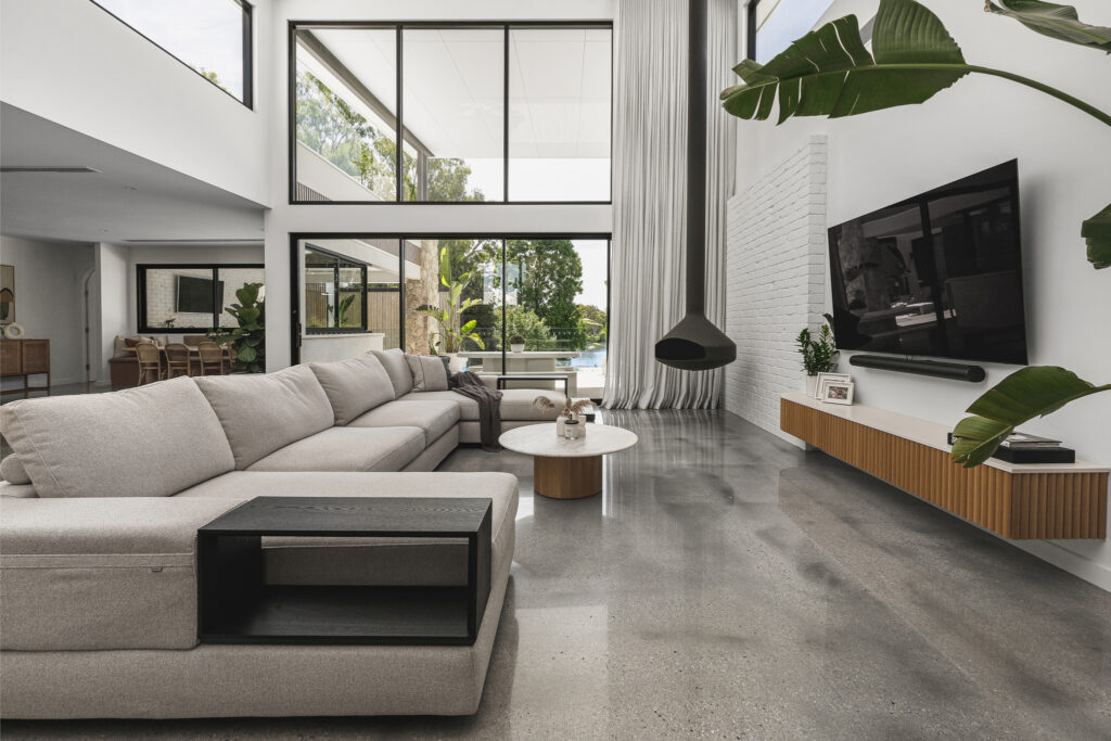 Modern living room with large windows, Caesarstone<sup>®</sup> TV unit benchtop, polished concrete floors, and neutral furnishings.