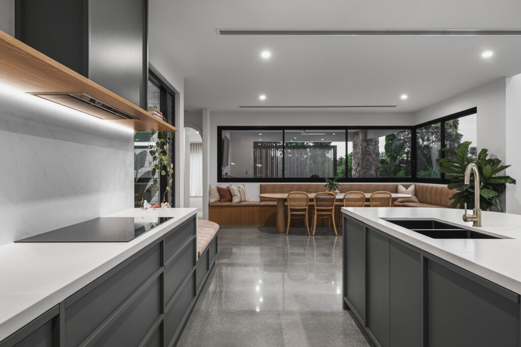 Contemporary kitchen featuring Caesarstone<sup>®</sup> benchtops and splashback, dark joinery, timber shelf detail, and built-in dining nook.