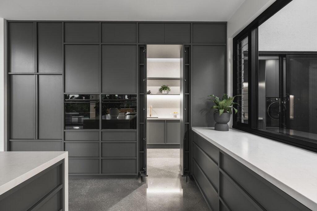 Contemporary kitchen featuring Caesarstone<sup>®</sup> benchtops and splashback, dark joinery, timber fluting detail, and built-in window seat.