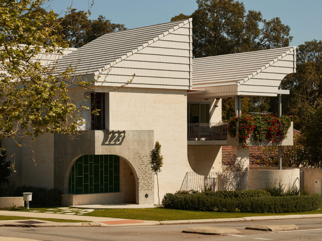 Contemporary residential exterior with sculptural rooflines, curved concrete entryway and lush greenery, showcasing modern Australian architecture by Neil Cownie.
