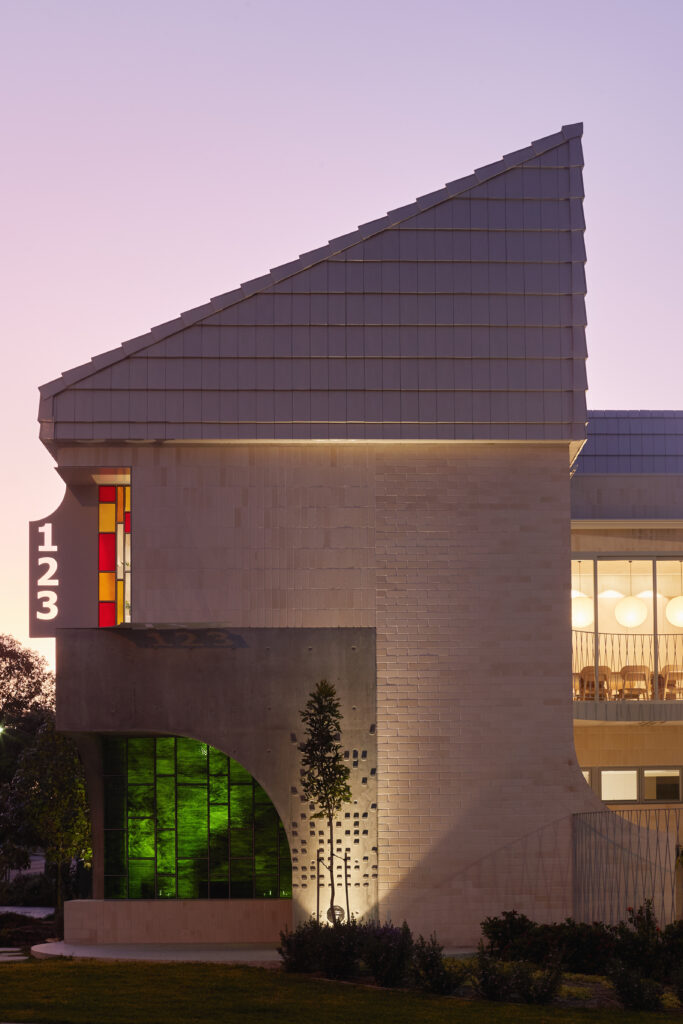 Exterior of 123 House at dusk, showcasing mid-century inspired form, arched concrete facade, and vertical coloured glass detail illuminated by evening light.