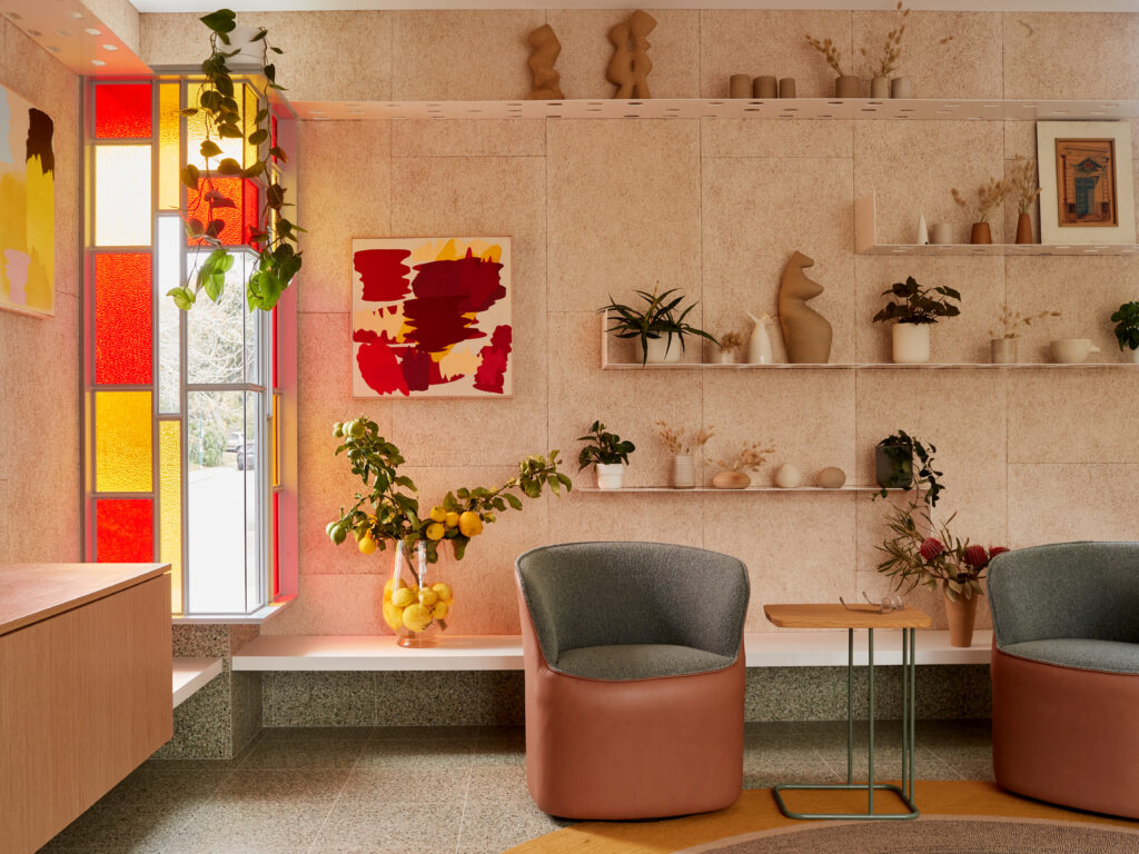 Living area featuring coloured glass window panels, terrazzo flooring, built-in shelving, indoor greenery, and mid-century inspired decor.