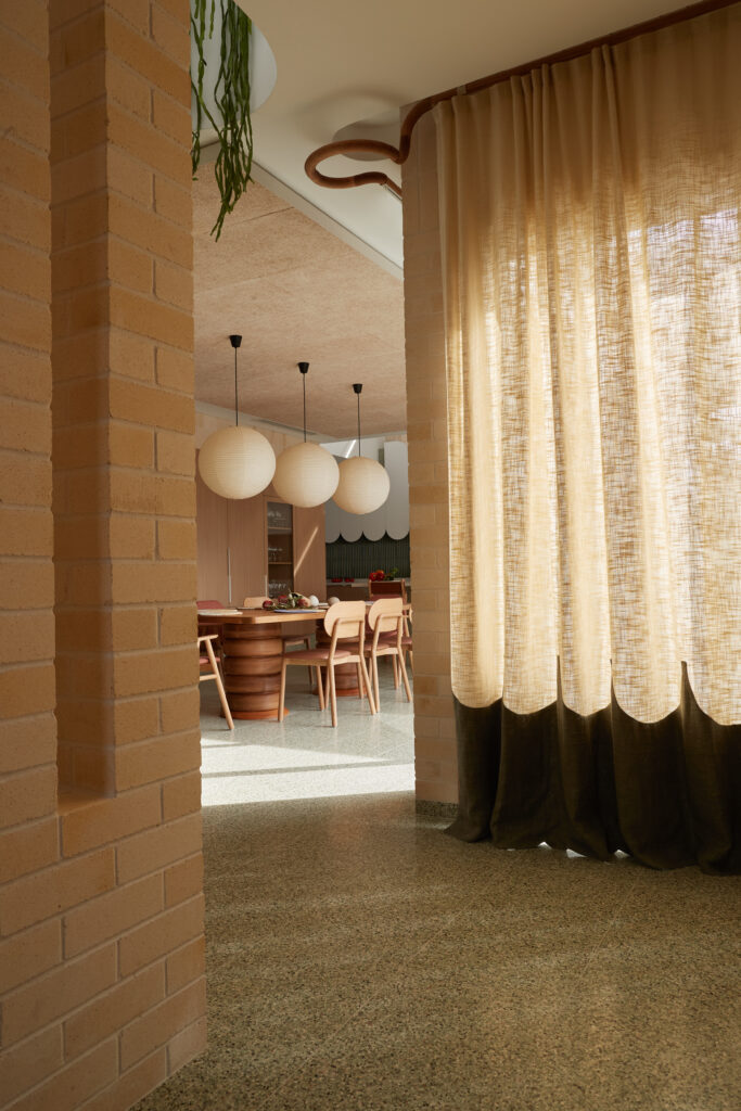 Soft-filtered light through custom curved timber curtain rail and linen drapes, leading to the dining area with terrazzo floors