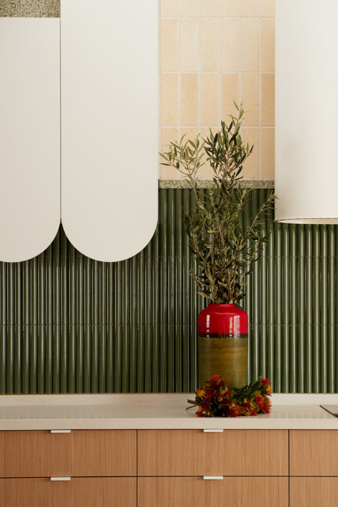 Detail of the kitchen, featuring Caesarstone<sup>®</sup> ICON™ benchtop, fluted green tile splashback, and sculptural white cabinetry.
