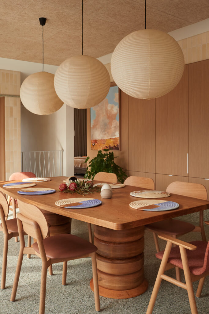 Dining area with custom circular timber table, terrazzo flooring, paper lantern pendants, and mid-century inspired cabinetry.