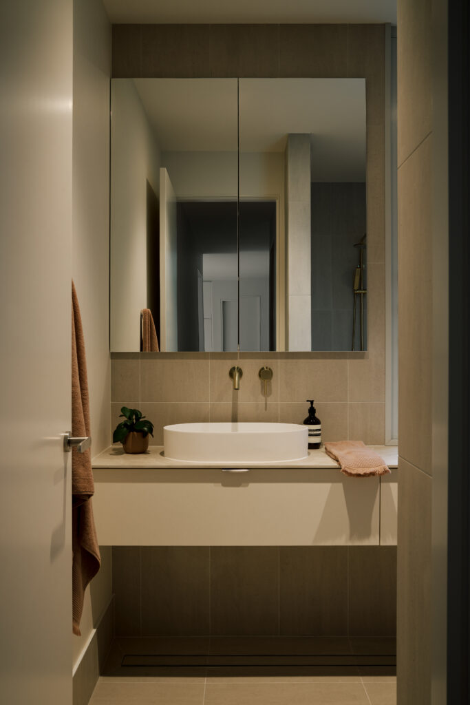 Bathroom featuring Caesarstone<sup>®</sup> Porcelain vanity benchtop with twin basins, brass tapware, and soft neutral tiles.