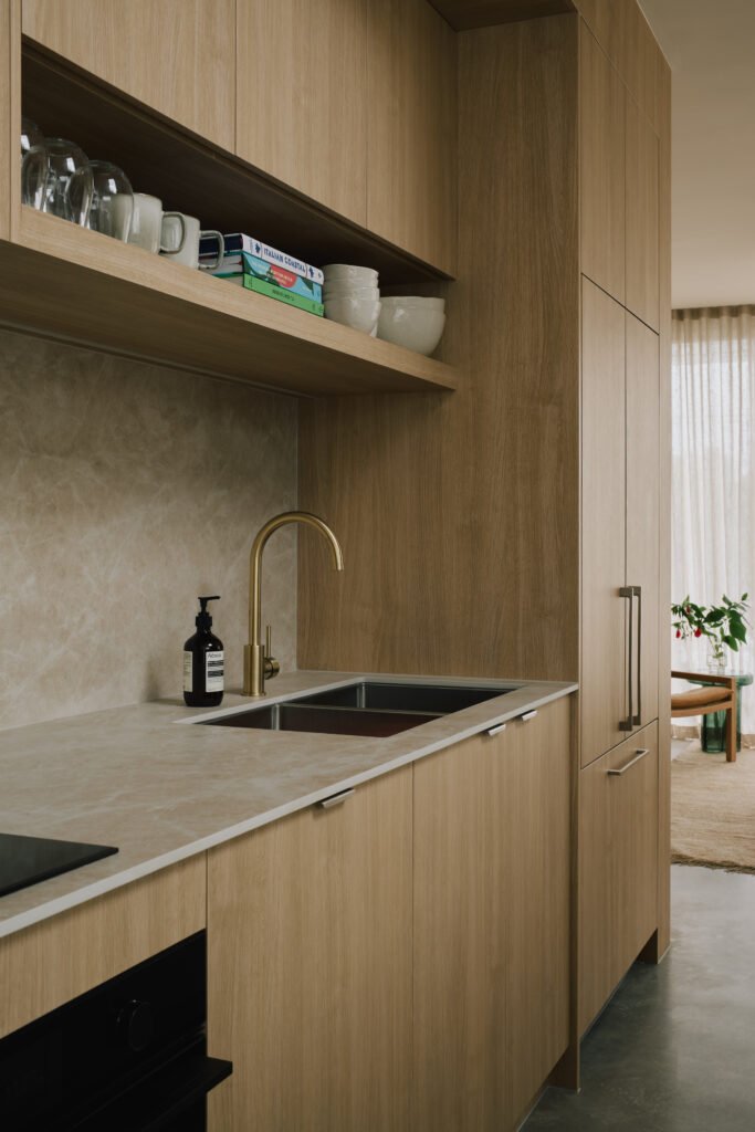 Kitchen detail showing Caesarstone<sup>®</sup> Porcelain benchtop and splashback with brass tapware and oak joinery.