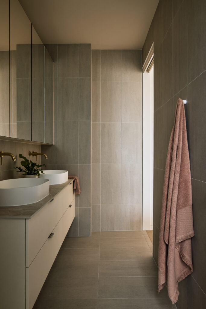 Bathroom featuring Caesarstone<sup>®</sup> Porcelain vanity benchtop with twin basins, brass tapware, and soft neutral tiles.