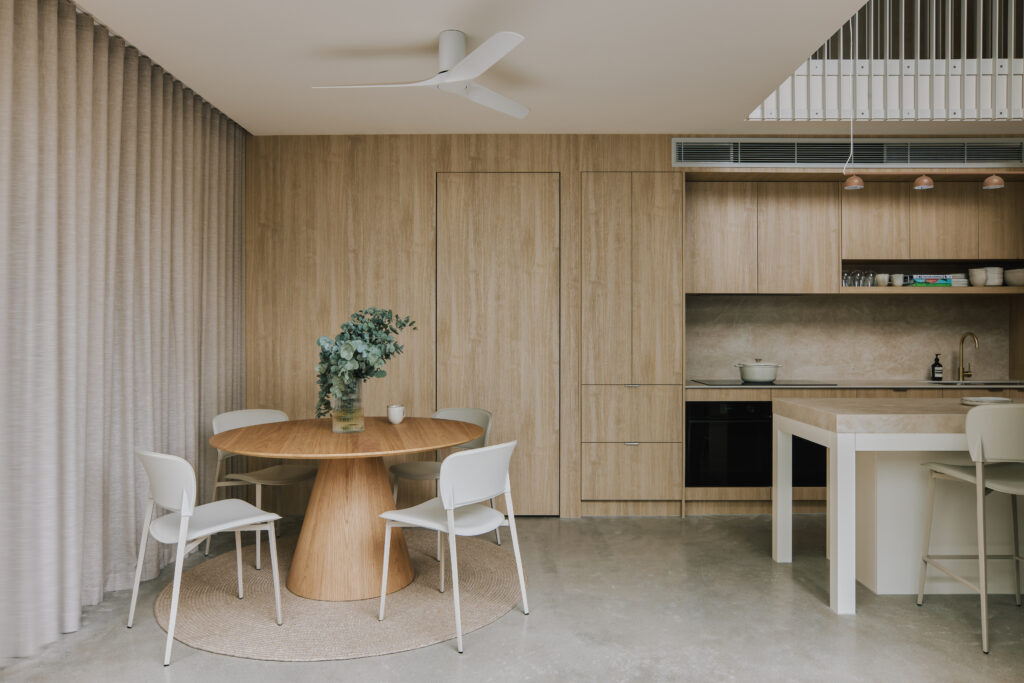 Open-plan dining and kitchen area featuring Caesarstone<sup>®</sup> Porcelain benchtop, timber joinery, and round oak dining table with neutral styling.