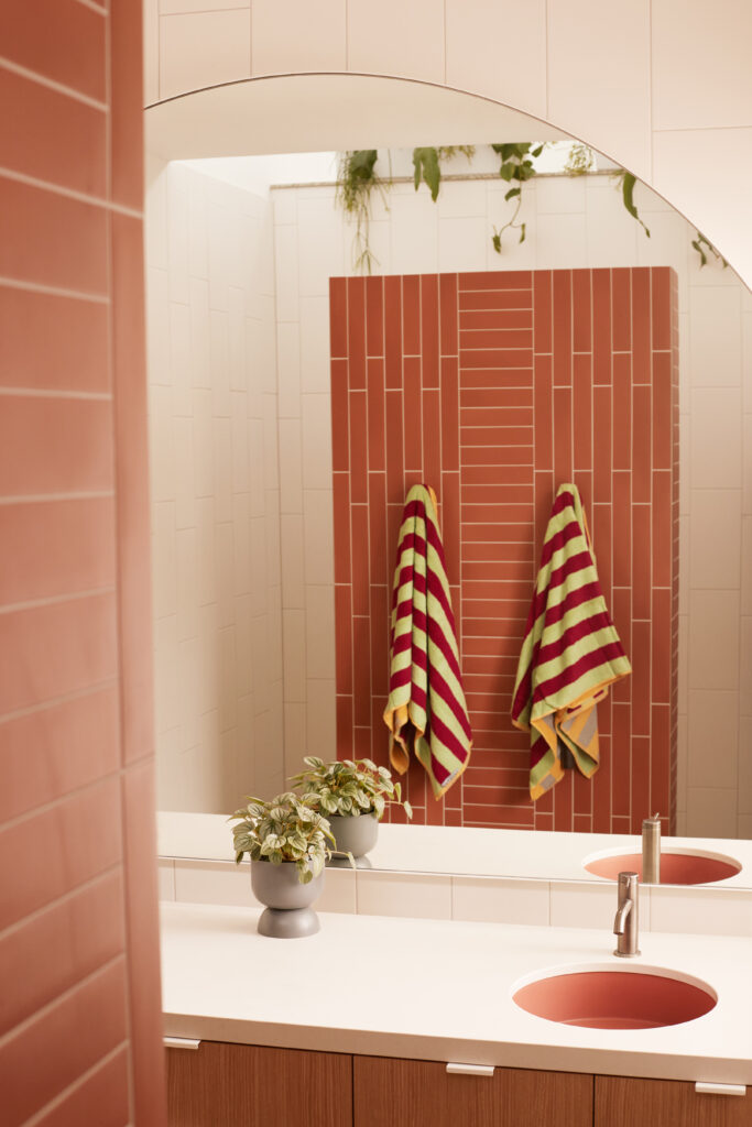 Bathroom vanity with Caesarstone<sup>®</sup> ICON™ benchtop, pink basin, vertical terracotta tiles, and soft arched mirror detail.