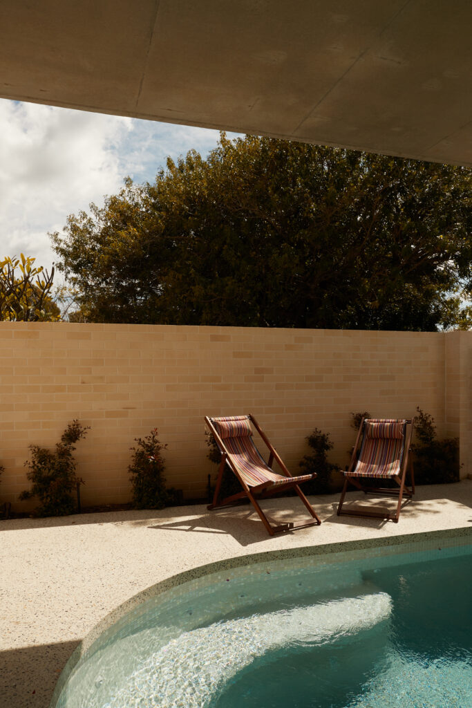 Private poolside courtyard featuring curved concrete edges, brick boundary wall, and sunlit lounge chairs.