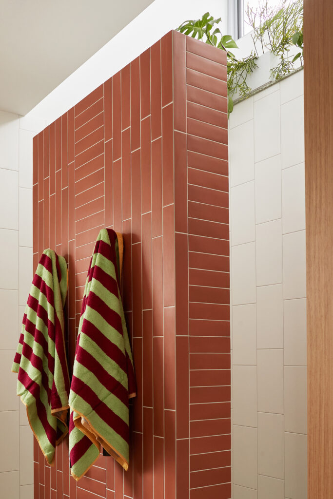 Bathroom walk-in-shower showcasing terracotta wall tiles, striped towels, and overhead greenery filtering natural light into the space.