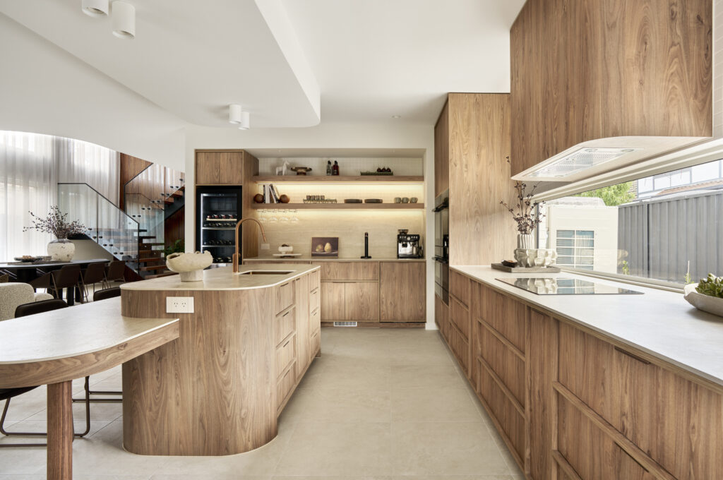 Curved kitchen island featuring Caesarstone Porcelain 550 Silvax benchtop with walnut cabinetry and brushed bronze tapware in The Kingscliff, Melbourne inner north west.
