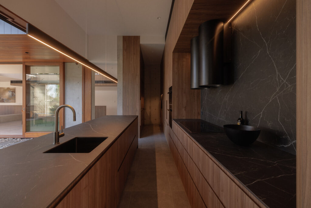 Kitchen with Caesarstone Smokestone Porcelain benchtops, black walnut cabinetry and brushed gunmetal fixtures at 56 Novus