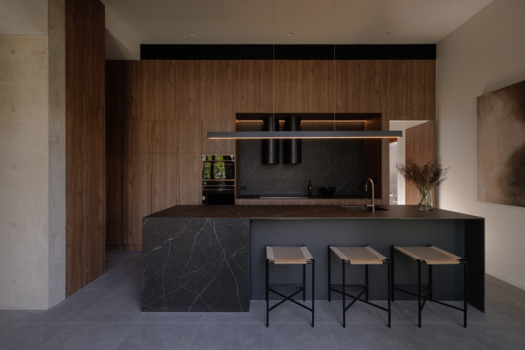 Kitchen island featuring Caesarstone Smokestone Porcelain benchtop with dark timber joinery, concrete walls and high ceilings at 56 Novus, Brisbane