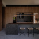 Kitchen island featuring Caesarstone Smokestone Porcelain benchtop with dark timber joinery, concrete walls and high ceilings at 56 Novus, Brisbane
