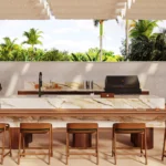 Caesarstone porcelain 536 Antikella in Outdoor kitchen with marble island, wooden stools, grill, sink, and tropical greenery background.