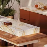 Caesarstone porcelain 536 Antikella in Modern outdoor kitchen with marble countertops, wooden bar stools, plants, and a built-in grill.