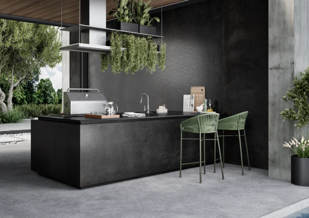 Caesarstone<sup>®</sup> Graphite Metal dark textured benchtop on freestanding outdoor kitchen island with green bar stools and concrete wall in modern Australian alfresco space